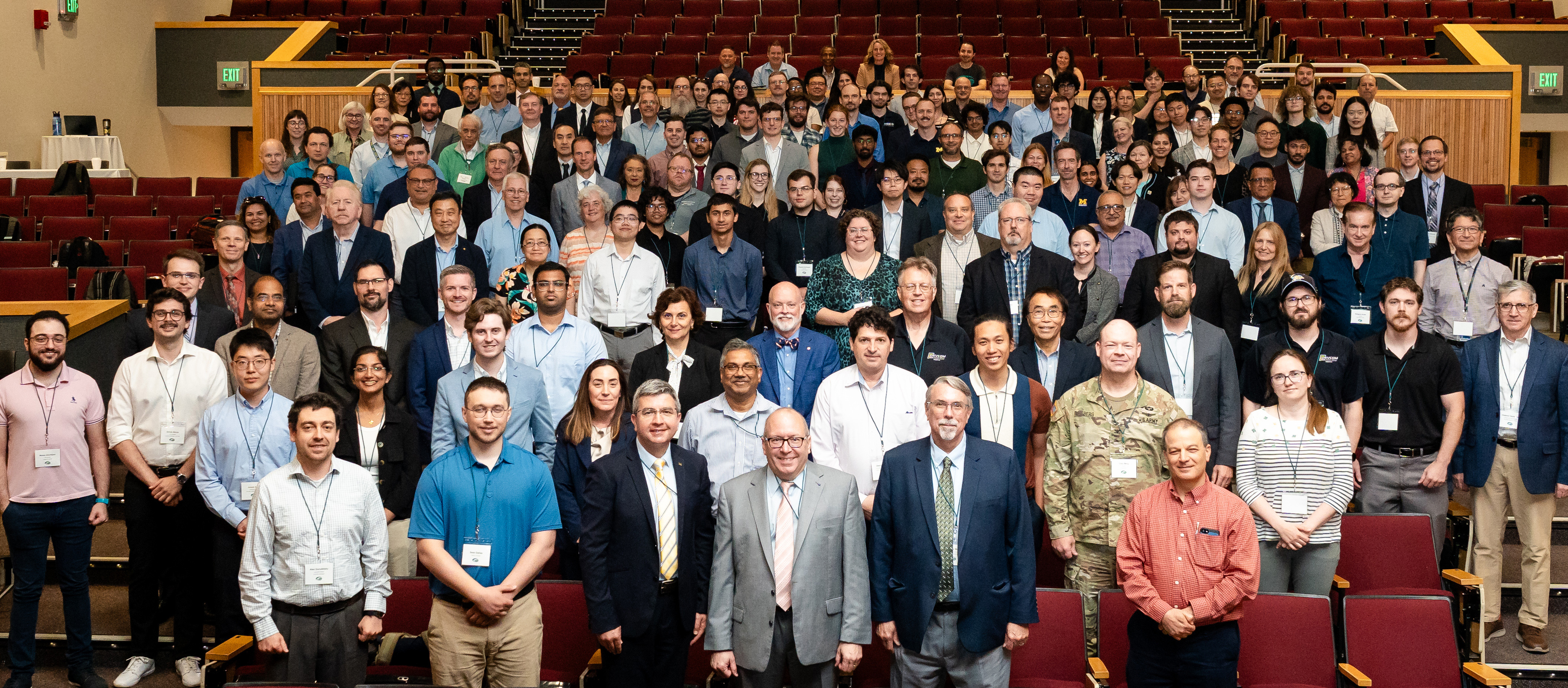 Group of 250 people, standing in auditorium, facing stage for group photo