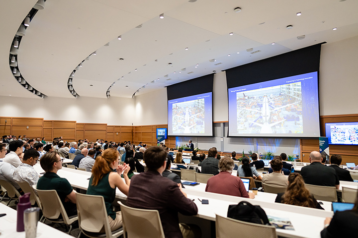 Boeing is advancing digital engineering and intelligent production systems to improve quality, precision, and efficiency across complex manufacturing operations. Photo Credit: Melanie Reyes Photography Dr. William Carter delivering keynote with a modern aircraft assembly facility on screen