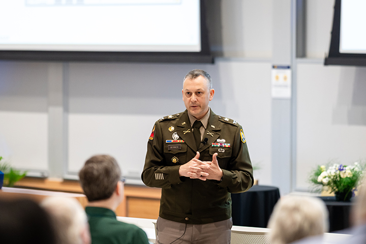Col. Bernier, wearing an Army uniform, delivers a keynote address to an audience.