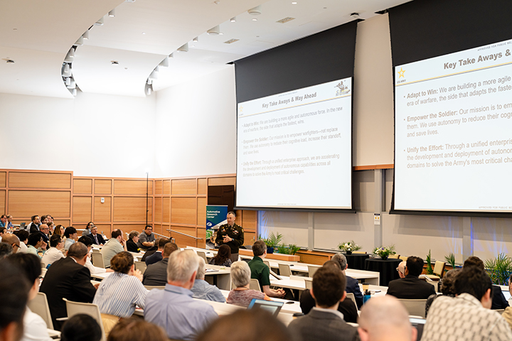 ARC research addresses many of the operational challenges highlighted during the Mission Autonomy keynote. Col. Bernier, wearing an Army uniform, delivers a keynote address to an audience seated in a room.