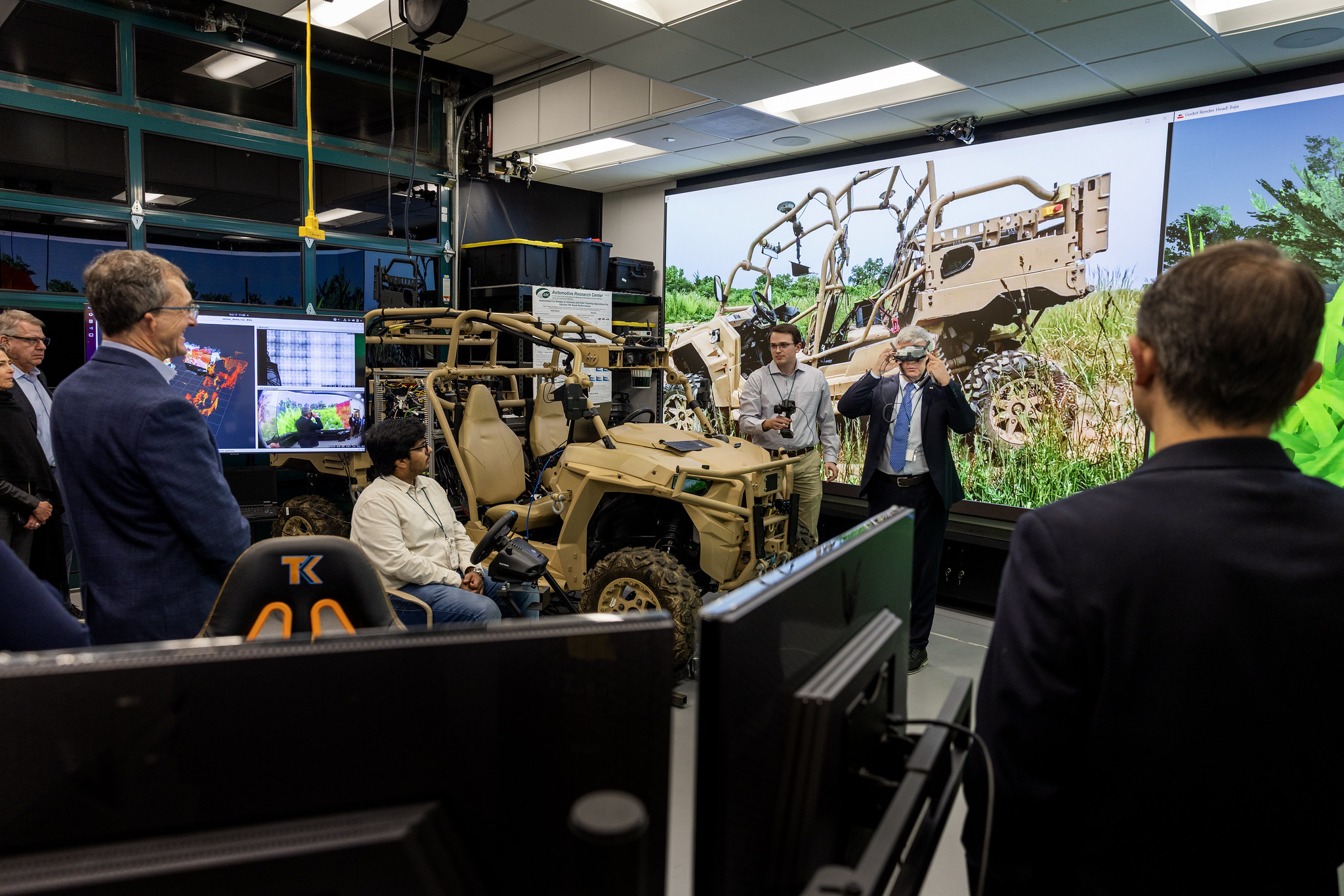 Prof. Bogdan Epureanu standing in front screen with video demonstrations of autonomous vehicles, wearing a headset with live camera feed. 