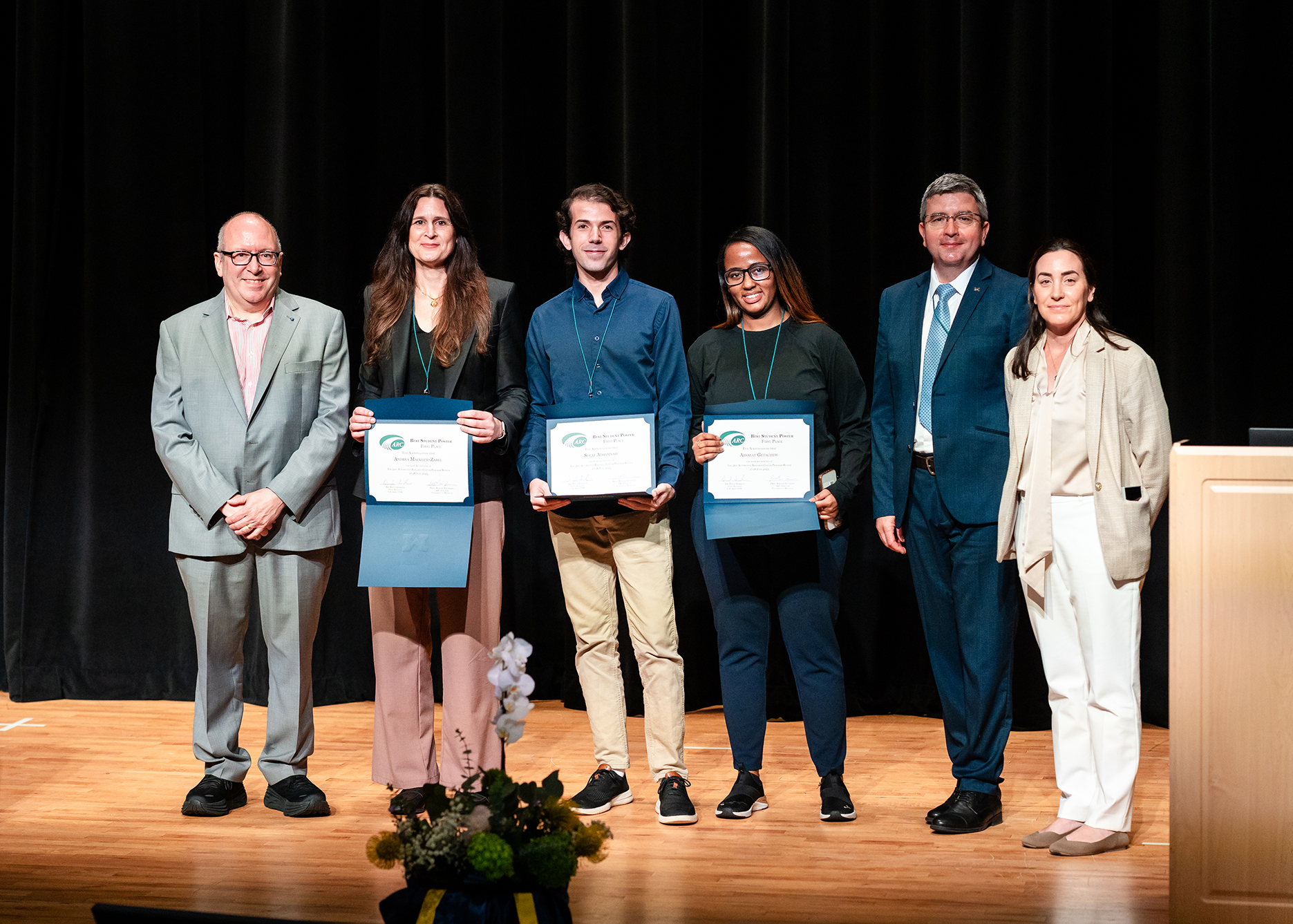 On stage from left to right: Dr. David Gorsich, Andrea Macklem-Zabel, Solaf Athamnah, Absalat Getachew, Prof. Bogdan Epureanu, and Dr. Talia Sebastian, standing in front of a black curtain.